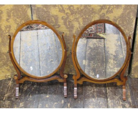 A close matched pair of Georgian style toilet mirrors in walnut, the oval mirror plates within skeleton frames