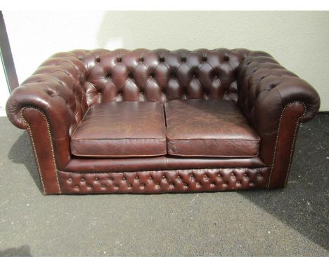 A brown leather chesterfield two seat sofa, with buttoned rolled arms and back and studded borders