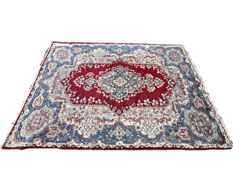 An old  Kirman carpet with a floral elongated medallion on a crimson field and blue floral borders 360cm x 250 cm approximate