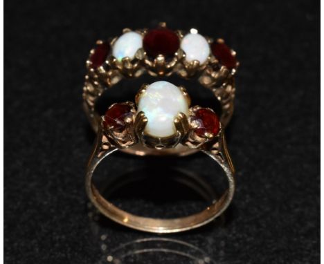 An opal and garnet trilogy ring, central oval creamy white opak flashing blue, green, violet and red colour play, flanked by 