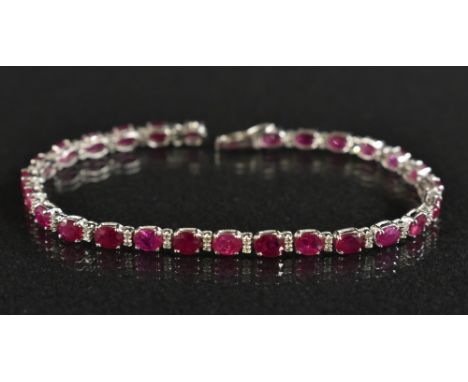 A diamond and ruby tennis bracelet, alternate set with twenty seven oval mixed cut pinky red rubies, each divided by a pair o