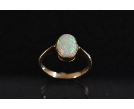 An 18ct gold ring, set with a single polished oval opal cabochon, flashing green, violet and orange colour play, stamped 18k,