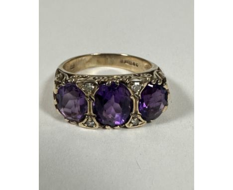 A 9ct Gold graduated three stone Amethyst and Diamond ring, the oval centre stone set with four diamond points mounted on ope