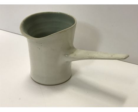 A Lucie Rie cream glazed pouring jug with side handle, with pale blue interior, bears Lucie Rie mark to base, 14 cm long x 8.