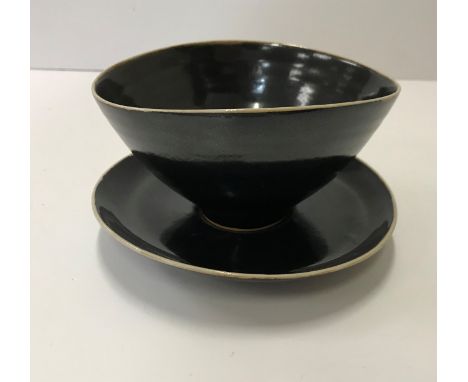 A Lucie Rie black glazed elliptical bowl and saucer, both bearing Lucie Rie marks, the bowl 12 cm x 14.5 cm x 7.5 cm high, th