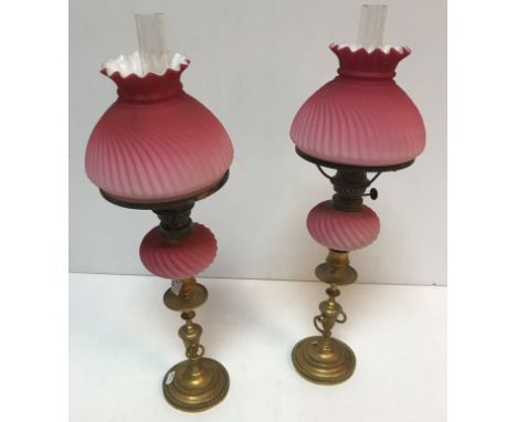 A pair of Victorian brass and cranberry glass oil lamps by Veritaslamp Works London, 51 cm high including funnel CONDITION RE