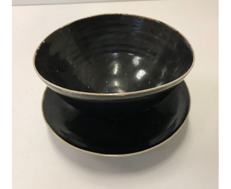 A Lucie Rie black glazed elliptical bowl and saucer, both bearing Lucie Rie marks 14 cm x 12.5 cm x 7.5 cm high, saucer 15.5 