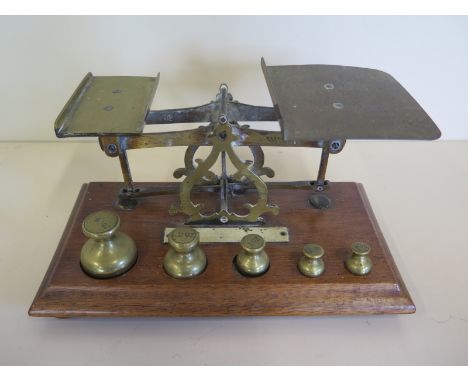 A set of brass postal scales with letter rates, set of plumb weights from half oz to 4 oz - with an oak base 
