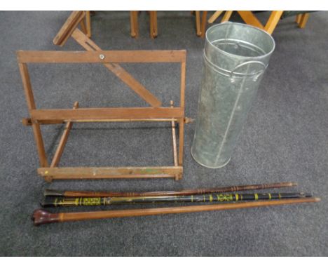 A folding wooden artists easel together with a metal stick pot containing three walking sticks.