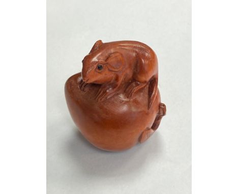 A carved fruitwood netsuke - rat seated on fruit