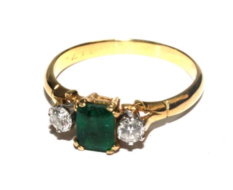 An 18 carat gold ring set with a trap cut emerald flanked by two diamonds 