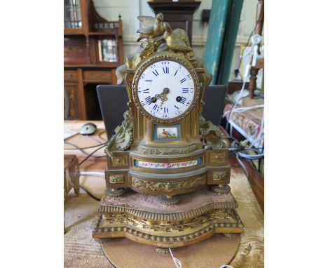 A French gilt metal and porcelain mounted mantel clock, deipicting musical instruments, armour and two doves, the twin train 