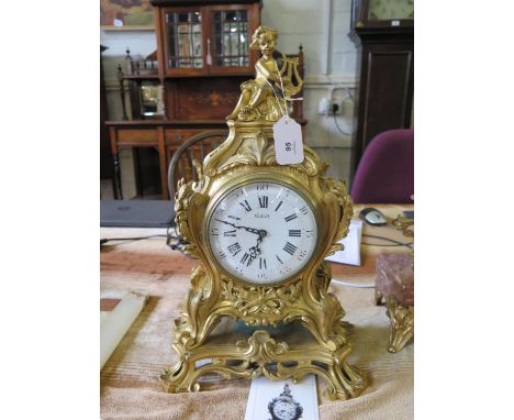 A French gilt metal mantel clock case, the putti playing a harp over foliate scrolls and flaming torches on a scrolling base,