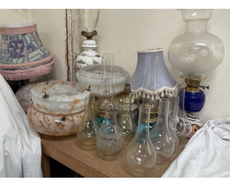 An oil lamp with a blue glass reservoir, together with other oil lamps, glass lamp shades, table lamps