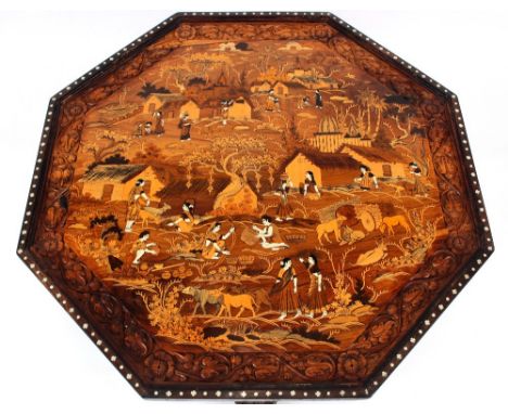 An Eastern carved and inlaid octagonal low table,&nbsp;profusely decorated with scenes of village life, raised on elephant tr