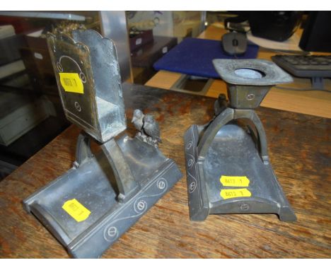 An Arts and Crafts pewter candlestick and matchbox holder, each supported on an arching twin column, the bases both sporting 