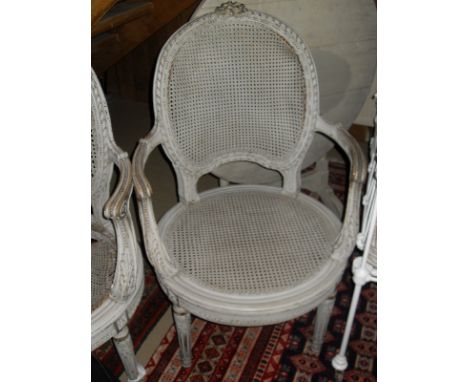 A two seat sofa and two armchairs with caned backs and seats in the French taste, painted cream, together with a torchere and