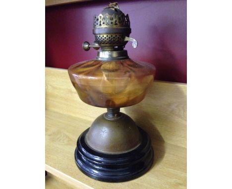 A vintage oil lamp with orange glass reservoir - no chimney.