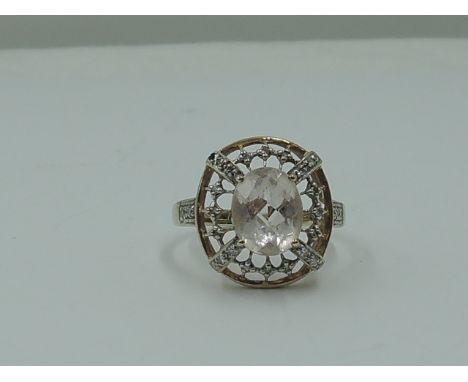 A lady's dress ring having a morganite style oval stone within an open border having diamond chip decoration on a 9ct gold lo