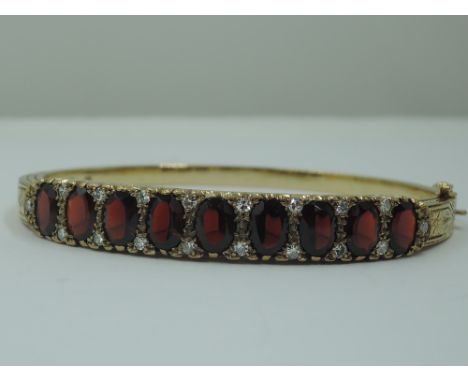 A 9ct gold hinged bangle set with nine oval garnets interspersed by pairs of diamond chips in a moulded gallery style mount, 