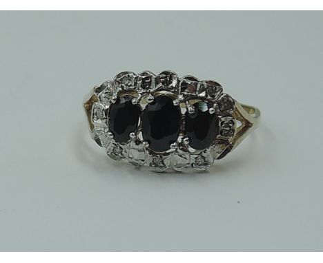 A lady's dress ring having a trio of oval sapphires within a diamond chip set illusionary surround to open shoulders on a 9ct