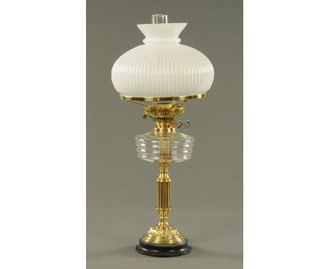 A Victorian brass oil lamp, with clear glass reservoir, milk glass shade and slate base.  Height including chimney 63 cm. 