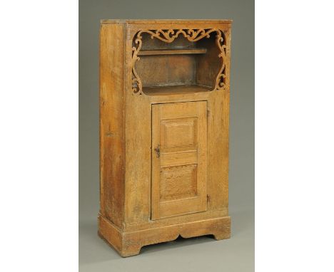 A rustic oak cupboard, late 19th century, the top opening to a single shelf and framed by pierced scrollwork decoration above