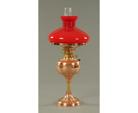A copper oil lamp, with integral reservoir and red mushroom shaped shade.  Height including reservoir 60 cm. 