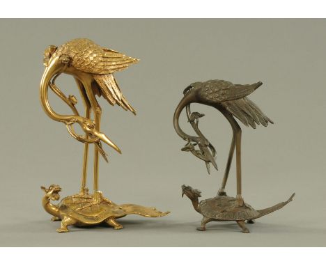 Two Japanese bronze Manchurian cranes, late Meiji period, each with a lily frond in its beak and standing on a snarling Minog