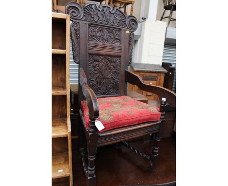 A Victorian oak wainscot armchair, in the 17th Century manner, with a scroll carved crest rail, panelled back, plank seat, ra