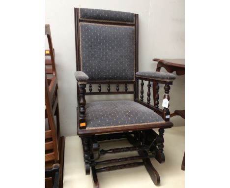 A late Victorian rocking chair, with an American style rocking mechanism, the padded back and padded arms with spindle galler