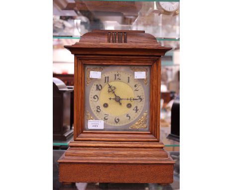 An oak mantel clock having silvered dial, with raised gold patterning to the corners, Arabic numerals, pendulum but no key  