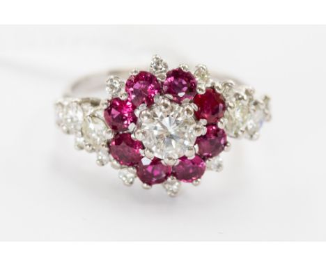 A diamond and ruby cluster ring, the central round brilliant cut diamond approx. 0.75 ct, a surround of rubies with diamond b