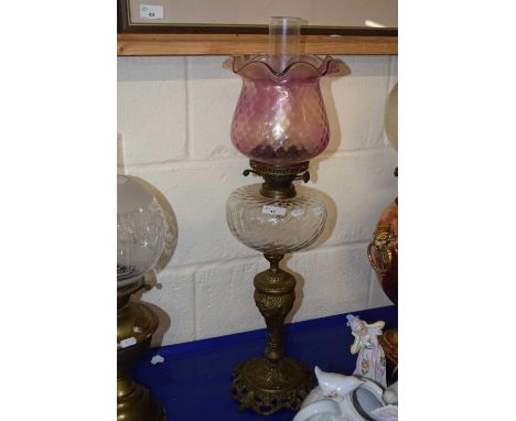 A brass based oil lamp with clear font and pink tinted frilled shade