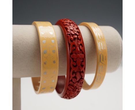 A trio of vintage bangle bracelets including one finely carved red cinnabar bangle featuring an ornate floral motif in high r
