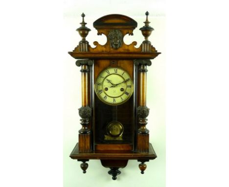A German Vienna style wall clock, in a walnut case, early 20th century, with a scroll top with finials, white enamel dial and