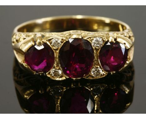 A three stone ruby and diamond carved head ring,with three graduated oval mixed cut rubies, with pairs of Swiss cut diamond s