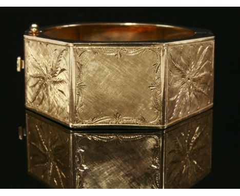 A flat section hexagonal hinged bangle, c.1960,with Florentine textured panels.  Each panel with hand engraved scroll border 