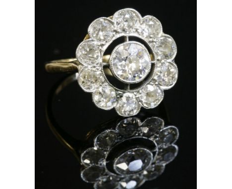 An Art Deco diamond set daisy cluster ring,with an old European cut diamond milligrain set to the centre.  An open frame to a