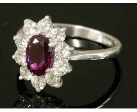 A white gold, ruby and diamond oval cluster ring,with an oval mixed cut ruby, four claw set to the centre.  Surrounded by bri