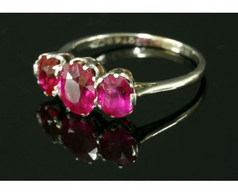 An Art Deco three stone ruby and synthetic ruby ring,with an oval mixed cut ruby to the centre and an oval mixed cut ruby and