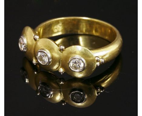 A three stone diamond ring,with three brilliant cut diamonds, all rub set to a white collet, to a textured disc surround.  Pa