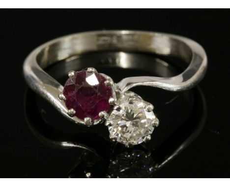 A white gold, two-stone ruby and diamond crossover ring,with a circular mixed cut ruby and a brilliant cut diamond, claw set 