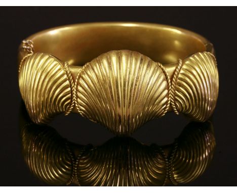 A Victorian hinged gold bangle,of oval elliptical form.  Three graduated clam shells to the top half, the central one hinged 