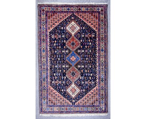 An Early 20th Century Shiraz Rug woven in colours of ivory, navy blue and wine, with five hooked octagonal guls, the field fi