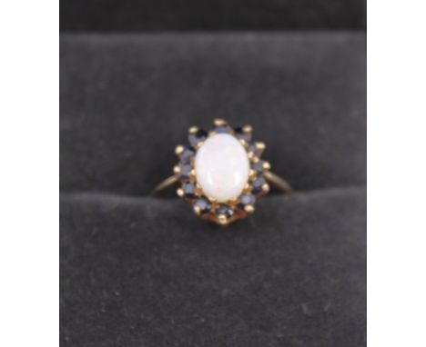 A 9ct Yellow Gold Opal and Sapphire Ring. The Oval Cabochon Opal measures approx. 8.36mm x 6.16mm. x 3mm depth.  There is twe