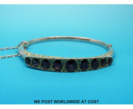 An Edwardian yellow metal bangle set with graduating oval garnets with alternating rose cut diamonds 