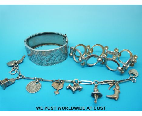 A large white metal bangle, a silver charm bracelet with nine charms including dogs and another silver bracelet