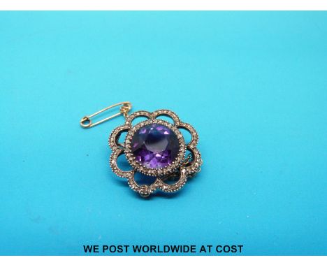 A yellow metal brooch set with an amethyst surrounded by diamonds