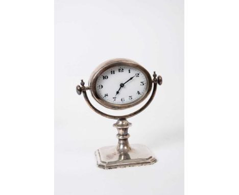 George V silver gimble desk clock on square base with shaped corners, knopped stem and oval clock with white enamel dial (Bir